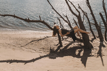 Portrait of an attractive woman in a black dress sits on the sand in the desert and the wind...