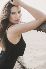 Portrait of an attractive woman in a black dress sits on the sand in the desert and the wind...
