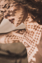 Portrait of a beautiful woman with long hair in abstract shadows on the background of sand in the desert. Fashion art shooting in gold color with lace and shadows on the face
