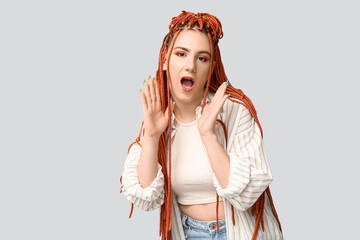 Portrait of pretty young woman with dreadlocks shouting on grey background
