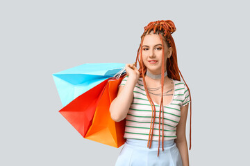 Portrait of pretty young woman with dreadlocks and shopping bags on grey background