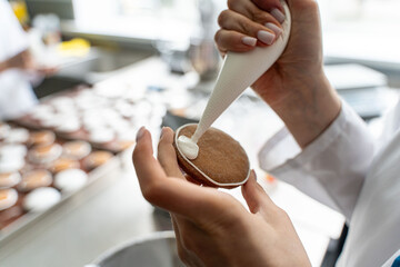 Close-up: Hands of a female pastry chef decorating cookies with white icing while squeezing cream out of a piping bag