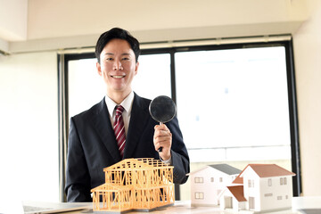 建築模型の前で虫眼鏡を持つスーツ姿の男性