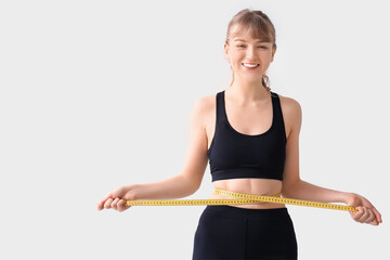 Beautiful young sporty woman measuring her waist on grey background. Weight loss concept