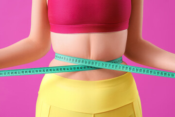 Young sporty woman measuring her waist on purple background. Weight loss concept