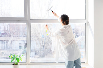 Young pregnant woman cleaning window at home