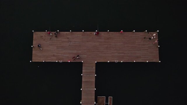 Drone top down descend on wooden T shaped pier dock with fishermen on edges