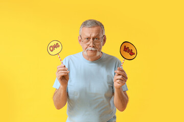 Shocked senior man holding speech bubbles with words WOW and OMG on yellow background