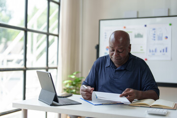 Happy African American businessman working with documents, preparing reports or marketing analysis, financial calculations. Working on a laptop computer online Contacting customers in a modern office