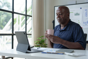 Senior African American businessman drinking coffee using laptop computer during cup break Relax at work in the office successful entrepreneur Independent businessman in the elderly.