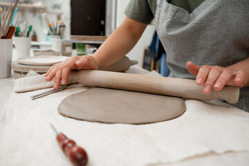 Rolling wooden stick to make flat sheet of clay. Preparing clay for cutting and assembling it. Slab...