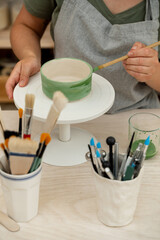 Girl is decorating a clay product with bright green color. Using a brush to paint a ceramics bowl. Learning how to paint a handmade pottery project.