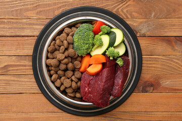 Bowl with healthy dry pet food, meat and vegetables on brown wooden background