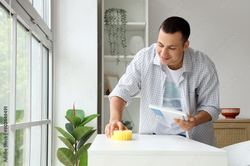 Poster Young man cleaning table with sponge at home