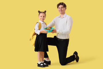 Fototapeta premium Little girl with school lunchbox and her father on yellow background