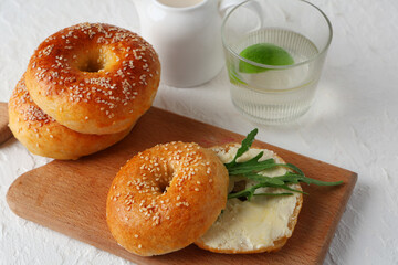 Wooden board of tasty bagels with butter and arugula on white background