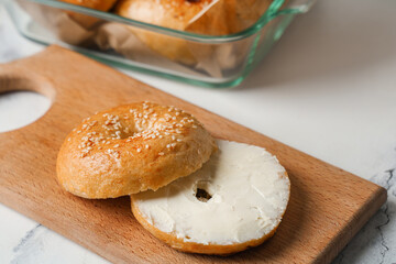 Wooden board of tasty bagel with butter on white background