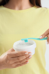 Young woman with tooth powder and brush on light background, closeup