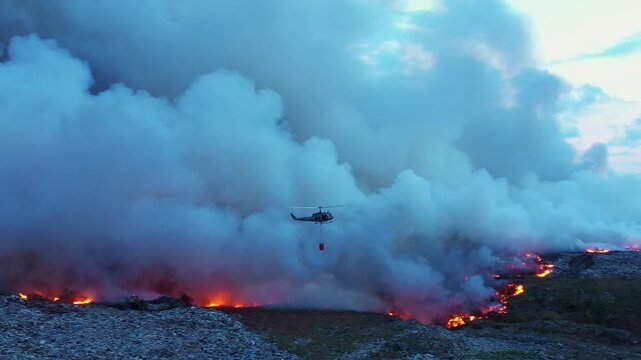 Fire control helicopter dropping water on bushfire, dark dusk evening in Australia - Aerial panoramic drone shot.