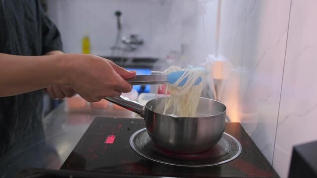Chef cooking white soba pasta with stirring the noodles with special tongs in a pan in the kitchen asian restaurant, close-up. Slow motion.