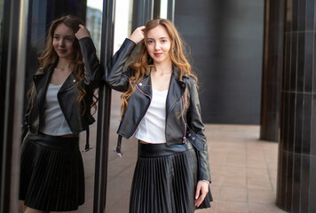 A young smiling girl in a good mood walks around the city. Teenage girl, portrait against the background of houses and roads. Fashionable youth style trend.
