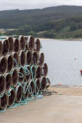 A large stack of cylindrical fishing traps is neatly arranged beside a waterfront dock, ready for...