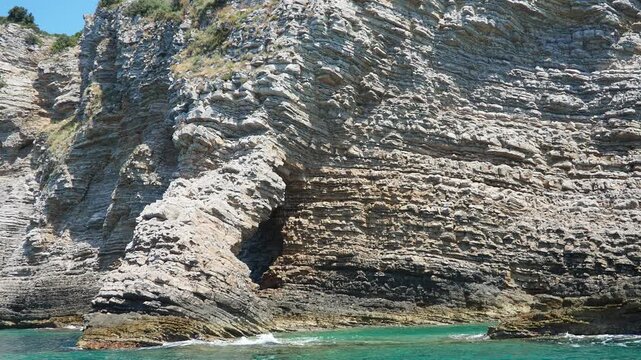 Cave Pecin bay near Seagull and Ratkova Kraljicina plaza Tri kralja. Hills, inaccessible rocks. Budva Montenegro. Flysch, marine sedimentary rocks, lithological layers. Adriatic Mediterranean sea