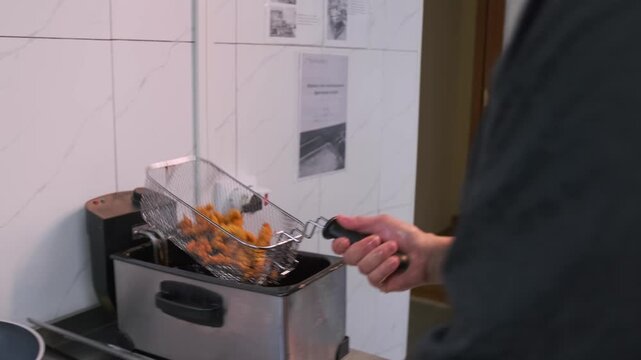 The chef shaking fried chicken wings in batter on the grill, while taking them out of the fryer letting the oil drain.