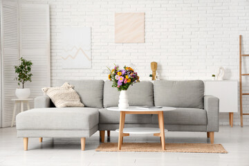 Comfortable sofa and vase with wild flowers on coffee table in interior of living room
