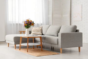 Comfortable sofa and vase with wild flowers on coffee table in interior of living room