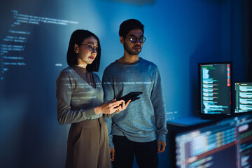 Asian Two software developers engaged in collaborative coding session, with code projected onto the...