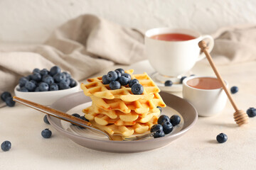 Delicious Belgian waffles with blueberries in plate on table against white background