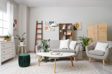 Interior of light living room with wooden ladder, sofa and armchair