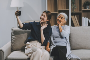 Obraz premium Cheerful mother and pretty teenager kid relaxing at cozy home, using mobile phone for Internet communication, resting on sofa with digital gadget, enjoying leisure, looking at camera