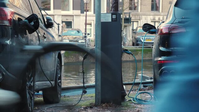 Urban electric vehicles are being powered, PHEV utilizing ecofriendly energy solutions. EV charging at a streetside station near a canal, showing sustainable urban transportation