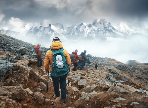 Group of backpackers walking down mountain trail with Himalayan mountains in background during trek in Langtang National Park, Nepal.