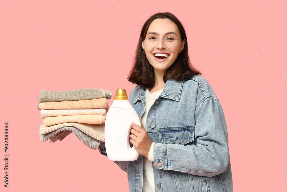 Canvas Prints Young woman with clean towels and bottle of detergent on pink background