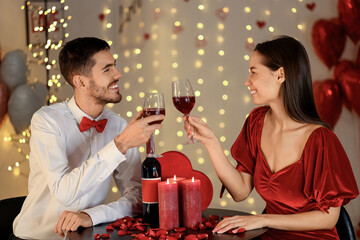 Young couple with glasses of wine having date at home decorated for Valentine's day celebration