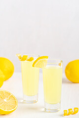 Homemade italian sweet limoncello liqueur made from zest of lemons served in shot glass decorated with citrus fruit slices as after dinner digestive on wooden table with ingredients and copy space