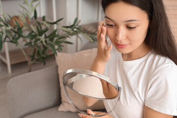 Young Asian woman with mirror putting in contact lenses in bathroom, closeup