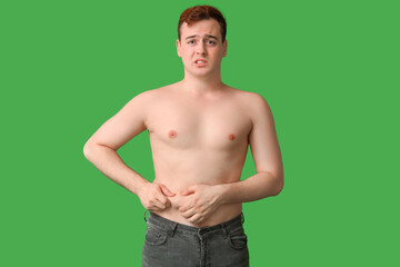 Young worried overweight man touching fat on his belly against green background. Weight gain concept