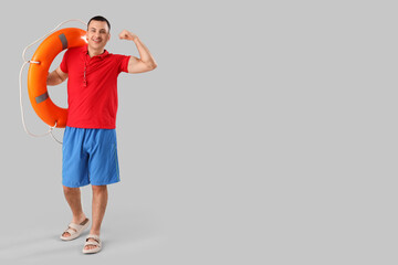 Happy male lifeguard with ring buoy showing muscles on grey background