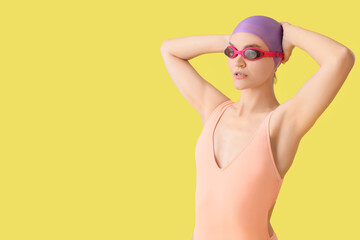 Professional young female swimmer on yellow background