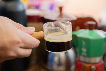 Barista preparing a coffee from moka pot coffee maker to a coffee cup.