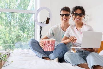 Couple of bloggers with popcorn and laptop recording review of movie in bedroom