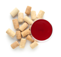 Glass of red wine and corks on white background