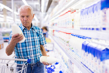 Elderly retired man buying milk in dairy section of the supermarket