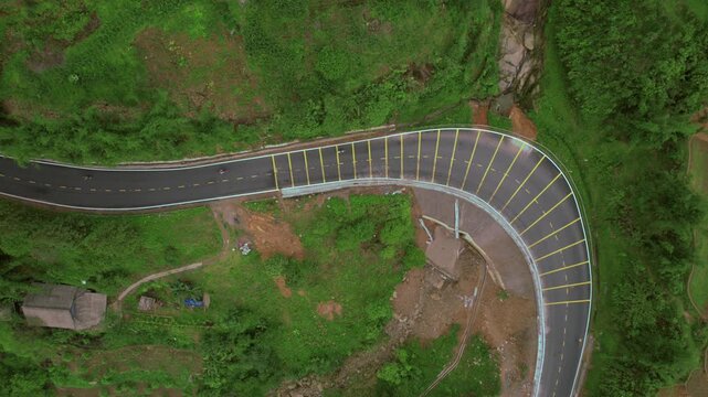 Tranquil Mountain Chicane: Aerial Drone View of Bicyclists on Scenic Road, Wood House, Rock Formation, and Lush Green Vegetation All Around