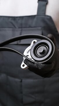 Auto mechanic holds auto parts, tension roller and poly V-belt. Auto parts concept and car maintenance, auto goods sales. Vertical. 