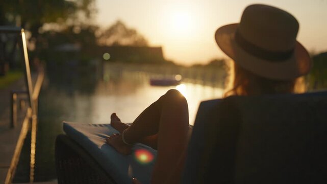 Calm summer evening in luxury hotel, woman lying on lounger, put hands back. Silhouette of lady tourist enjoying amazing sunset in luxury hotel, sexy female legs on deck chair, happiness and joy